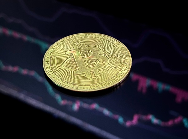 Gold Bitcoin coin on a dark screen with a price chart