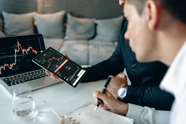 Two people reviewing market charts on a laptop and tablet