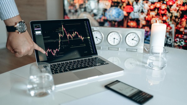 Hand pointing at a candlestick chart on a laptop