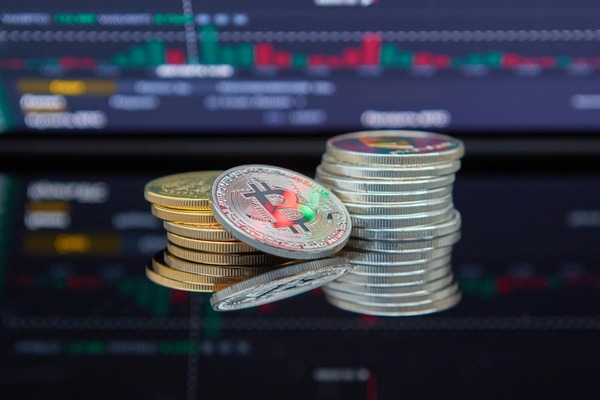 Stacks of crypto coins in front of a trading screen