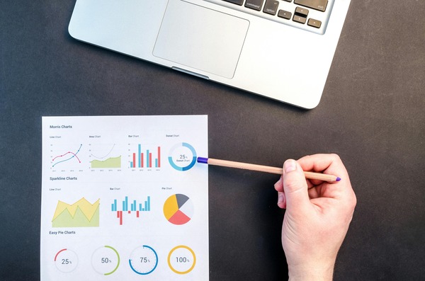 Hand pointing a pencil at printed charts next to a laptop