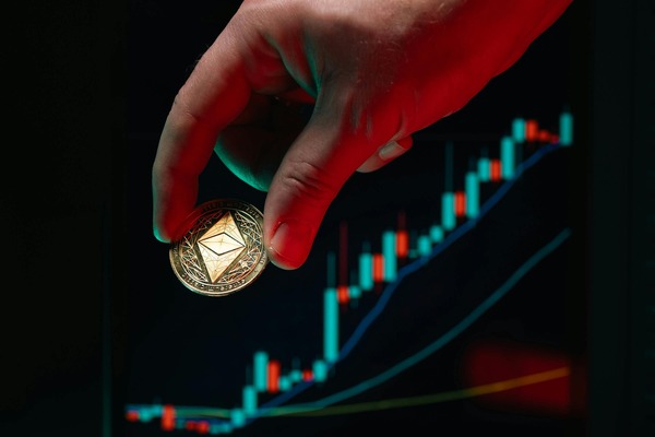 Hand placing an Ethereum coin on a rising price chart