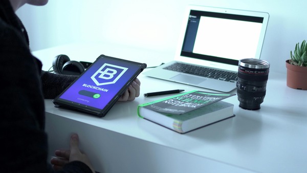 Tablet with a blockchain app on a desk beside a laptop