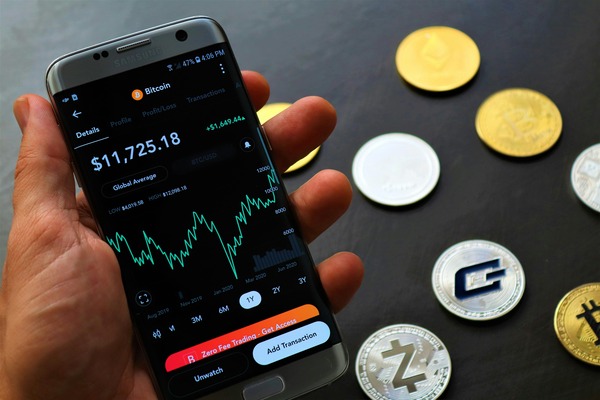 Hand holding a phone with a crypto price chart next to coins