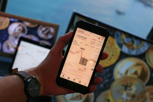 Hand holding a phone with a price chart above crypto coins
